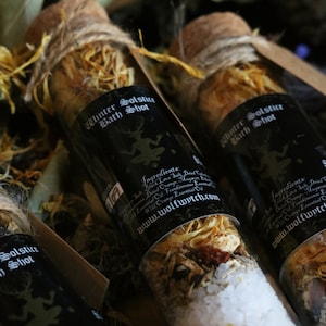 May include: Three glass bottles filled with dried herbs and bath salts. The bottles are labeled "Winter Solstice Bath Shot" and include a list of ingredients and the website "www.wolfwitch.com".