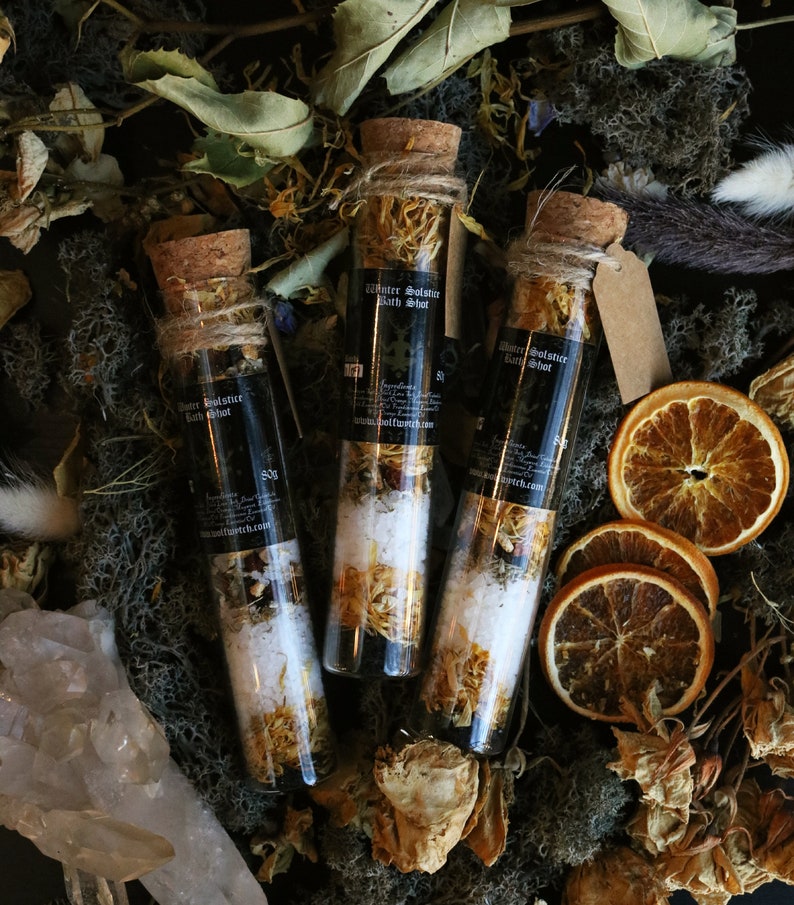May include: Three small glass bottles filled with bath salts and dried flowers. The bottles have cork stoppers and are labeled "Winter Solstice Bath Shot".