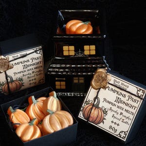 May include: A black house-shaped wax warmer with an orange pumpkin wax melt inside, and a box of orange pumpkin-shaped wax melts. The boxes are labelled "Pumpkins Past Midnight" with "Spooky Pumpkin Spiced Latte" scent.