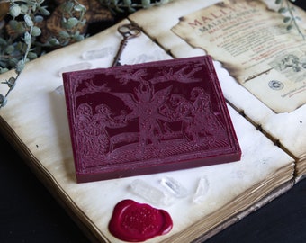 May include: A deep red wax seal with an intricate design of a winged figure and several other figures. The seal is on a vintage book with a page open to a text about "Malleus Maleficarum".