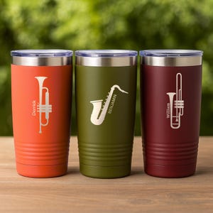 May include: Three insulated tumblers in orange, olive green, and burgundy. Each tumbler features a musical instrument design: a trumpet, a saxophone, and a trombone. The names "Derrick", "Benjamin", and "William" are printed on the tumblers.