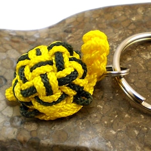 May include: A yellow and black paracord turtle keychain. The turtle is made with a knotting technique and is attached to a silver key ring.
