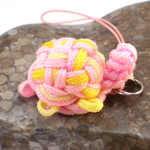 Può includere: Un ciondolo per telefono a nodo intrecciato rosa e giallo con un anello in metallo argentato.