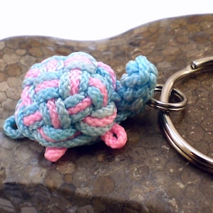 Op de afbeelding: Een roze en blauwe geknoopte schildpad sleutelhanger met een zilveren sleutelring.