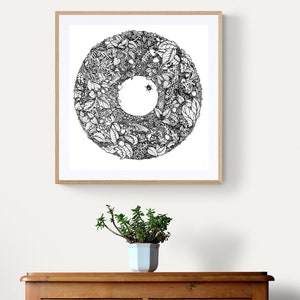K&ouml;nnte beinhalten: Gerahmte schwarz-wei&szlig;e botanische Illustration mit einem kreisf&ouml;rmigen Design aus Bl&auml;ttern, Beeren und einem Insekt. Das Kunstwerk h&auml;ngt an einer wei&szlig;en Wand &uuml;ber einer Holzkommode, mit einer Topfpflanze davor.
