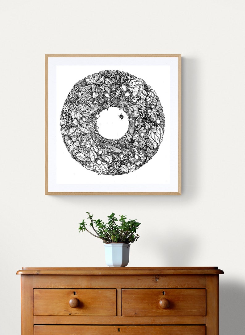 K&ouml;nnte beinhalten: Gerahmte schwarz-wei&szlig;e botanische Illustration mit einem kreisf&ouml;rmigen Design aus Bl&auml;ttern, Beeren und einem Insekt. Das Kunstwerk h&auml;ngt an einer wei&szlig;en Wand &uuml;ber einer Holzkommode, mit einer Topfpflanze davor.