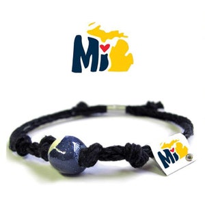 Peut inclure: Un bracelet en corde noire avec une perle bleu foncé et un fermoir argenté. Une petite étiquette avec le contour de l'État du Michigan et "Mi" en bleu et jaune est attachée. Un accessoire de mode fait main.