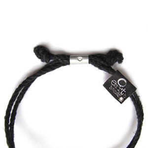 May include: Black cord bracelet with a silver heart charm and a black tag with the text "Orto Designs" in white.