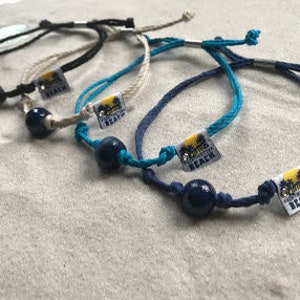 May include: Five colorful bracelets with a dark blue bead and a silver charm that says "California Beach".