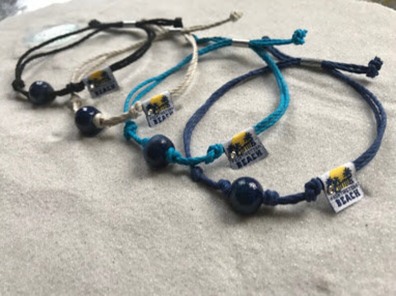 May include: Five colorful bracelets with a dark blue bead and a silver charm that says "California Beach".
