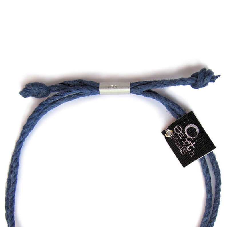 May include: A blue cotton cord bracelet with a silver adjustable slider and a black tag that reads "Orca Designs".