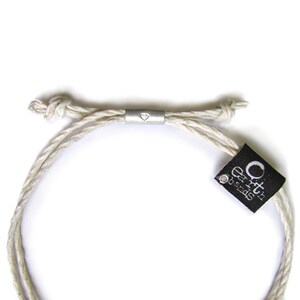 May include: A white braided cord bracelet with a silver heart charm and a black tag that reads "Earth's Treasures".