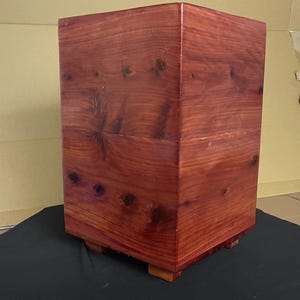 May include: A rectangular wooden box with a reddish-brown finish. The box has a slightly raised base and is made of cedar wood.