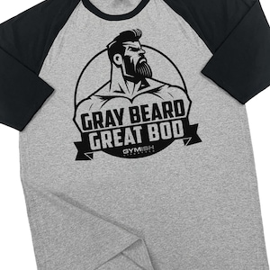 May include: Gray and black baseball tee shirt with a graphic of a muscular man with a gray beard. The graphic is inside a circle with the text "Gray Beard Great Bod" and "Gymish Lifestyle" underneath.