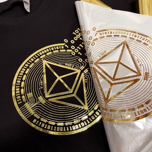 May include: A black t-shirt with a gold foil design of a geometric shape surrounded by a circle of binary code.