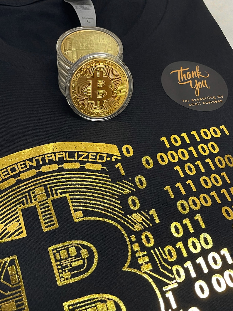 May include: Black t-shirt with a gold foil design of a circuit board and the text "DECENTRALIZED". The design also includes a gold foil Bitcoin symbol and binary code. The shirt has a thank you sticker with the text "Thank You for supporting my small business".