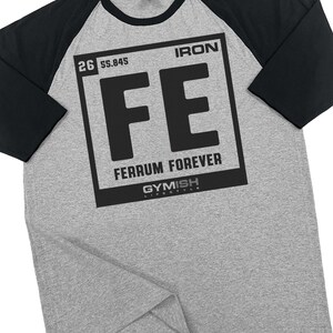 May include: A gray raglan-style t-shirt with black sleeves. The shirt features a black graphic of the periodic table symbol for iron, "FE", with the words "Ferrum Forever" and "Gymish Lifestyle".