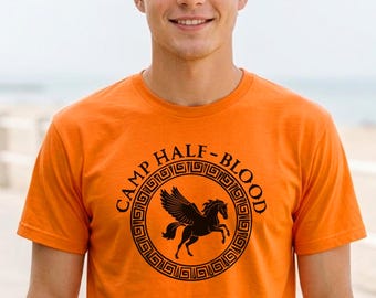 Può includere: Una t-shirt arancione a maniche corte con una grafica circolare nera sul petto. Il design presenta un cavallo alato al centro circondato da un bordo a greca e dal testo CAMP HALF-BLOOD stampato in un carattere nero e in grassetto.