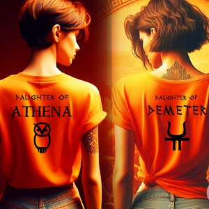 May include: Two women wearing orange t-shirts with Greek mythology designs. The first shirt says "Daughter of Athena" with an owl graphic. The second shirt says "Daughter of Demeter" with a trident graphic.
