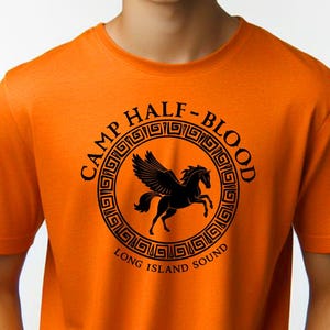 Könnte beinhalten: Orangefarbenes T-Shirt mit einer schwarzen Grafik eines geflügelten Pferdes in einem Kreis mit dem Text "Camp Half-Blood Long Island Sound".