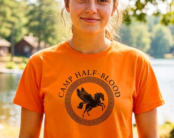 May include: A bright orange short-sleeved t-shirt featuring a black circular graphic on the chest. The design includes a winged horse in the center, surrounded by a Greek key border and the text CAMP HALF-BLOOD printed in a circular arc.