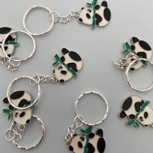 May include: A set of six keychains featuring panda bears holding bamboo stalks. The pandas are black and white with green bamboo stalks. The keychains are silver and have a circular shape.