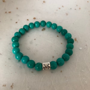 May include: Turquoise gemstone bracelet with a silver charm featuring the Taurus zodiac symbol.