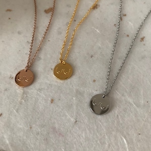 May include: Three necklaces with a round pendant featuring a stylized image of breasts. The necklaces are available in gold, rose gold, and silver.