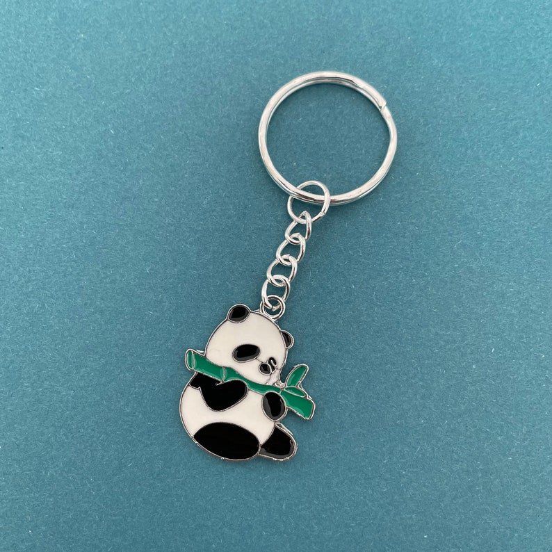 May include: A silver key chain with a black and white panda charm holding a green bamboo shoot.