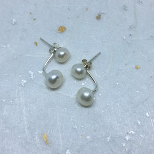 May include: A pair of silver earrings with two white pearls on each earring.