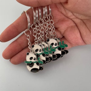 May include: A set of six silver keychains featuring panda bears holding green bamboo shoots. Each panda is outlined in black and has white fur with black eyes and ears.
