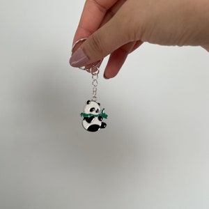 May include: A silver keychain with a black and white panda charm holding a green bamboo stalk.