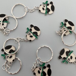May include: A set of six silver keychains featuring panda bear charms with green bamboo. Each keychain has a silver ring and a different panda bear design.