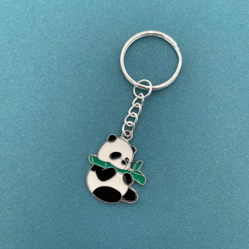 May include: A silver keychain with a black and white panda bear charm holding a green bamboo stalk.