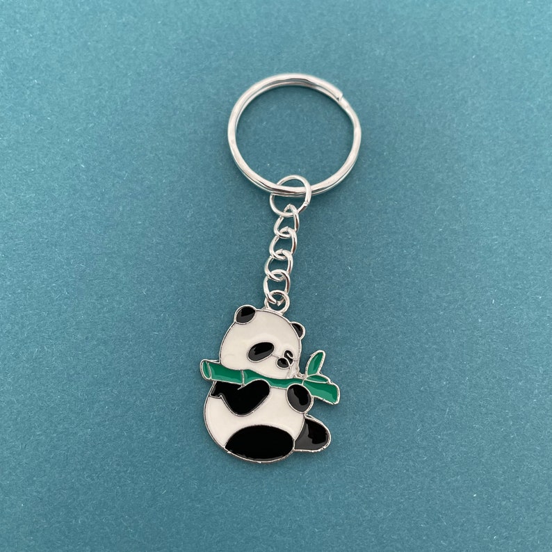May include: A silver keychain with a black and white panda holding a green bamboo shoot.