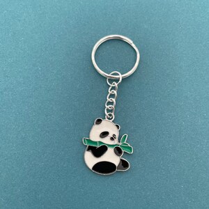 May include: A silver keychain with a black and white panda bear charm holding a green bamboo shoot.