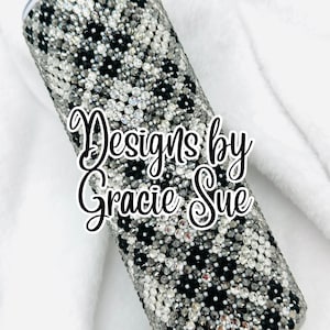 Puede incluir: Vaso cilíndrico cubierto de pedrería negra y plateada. El diseño presenta un patrón de manchas negras sobre un fondo plateado. El texto "Designs by Gracie Sue" está escrito en cursiva. El vaso es de acero inoxidable.