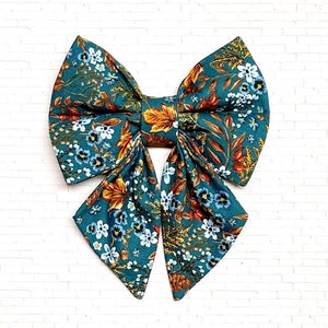 May include: A teal blue bow with a floral and leaf pattern. The bow has a large center bow and two long tails.