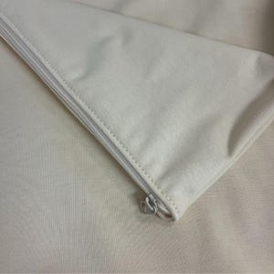 May include: A close-up of a zipper on a white fabric pouch. The zipper is silver and has a heart-shaped pull.