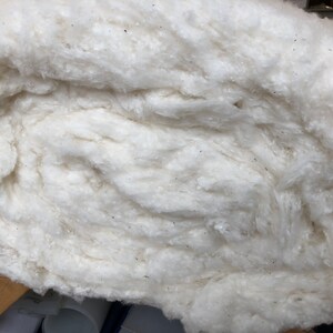 May include: A close-up of a large, fluffy, white cotton ball. The cotton is tightly packed together, creating a soft and textured surface.
