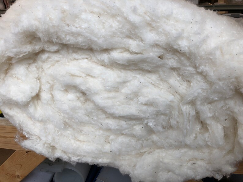May include: A close-up of a large, fluffy, white cotton ball. The cotton is tightly packed together, creating a soft and textured surface.