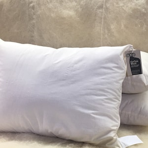 May include: A stack of four white pillows with a tag that reads "CeCe's Wool" on the top pillow.