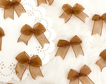 May include: A collection of brown, sheer ribbon bows arranged on a white surface. The bows are tied in a simple knot and have a delicate, feminine look.