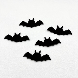 May include: A set of five black bat-shaped cutouts arranged in a scattered pattern. Each bat silhouette features pointed ears and outstretched wings with scalloped edges, creating a uniform dark shape against a plain white background.
