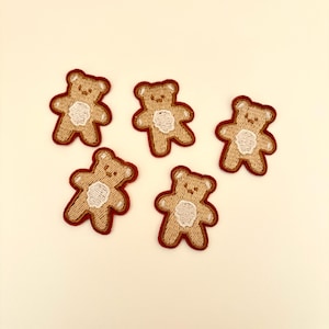 May include: Five brown embroidered iron-on patches of teddy bears with white faces. The bears are standing upright with their arms outstretched.