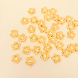 May include: A collection of small, yellow, embroidered flower appliques with white centers. The flowers are scattered across a light yellow background, creating a delicate and cheerful aesthetic. These appliques are suitable for various craft projects.