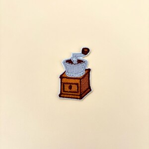 May include: A brown wooden coffee grinder with a silver metal grinder and a brown handle. The grinder is on a white background.