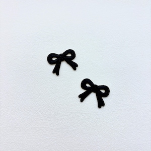 May include: Two small, black embroidered bow appliques featuring a detailed stitched texture. Each bow has two loops and two short, dangling ends, creating a classic knot shape. These decorative fabric patches are solid black in color.