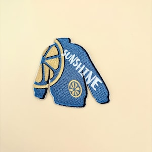 May include: Blue embroidered iron-on patch with a yellow lemon slice and the word "SUNSHINE" in white text.