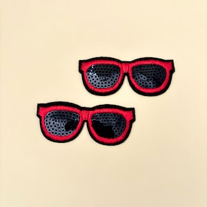 May include: Two red sequin sunglasses patches. The sunglasses are black with a red outline.
